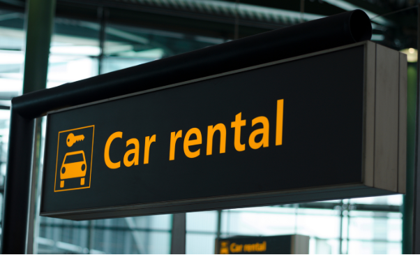 Car rental signage at a European airport as services adapt to EU border checks travel delays for non-EU travellers.
